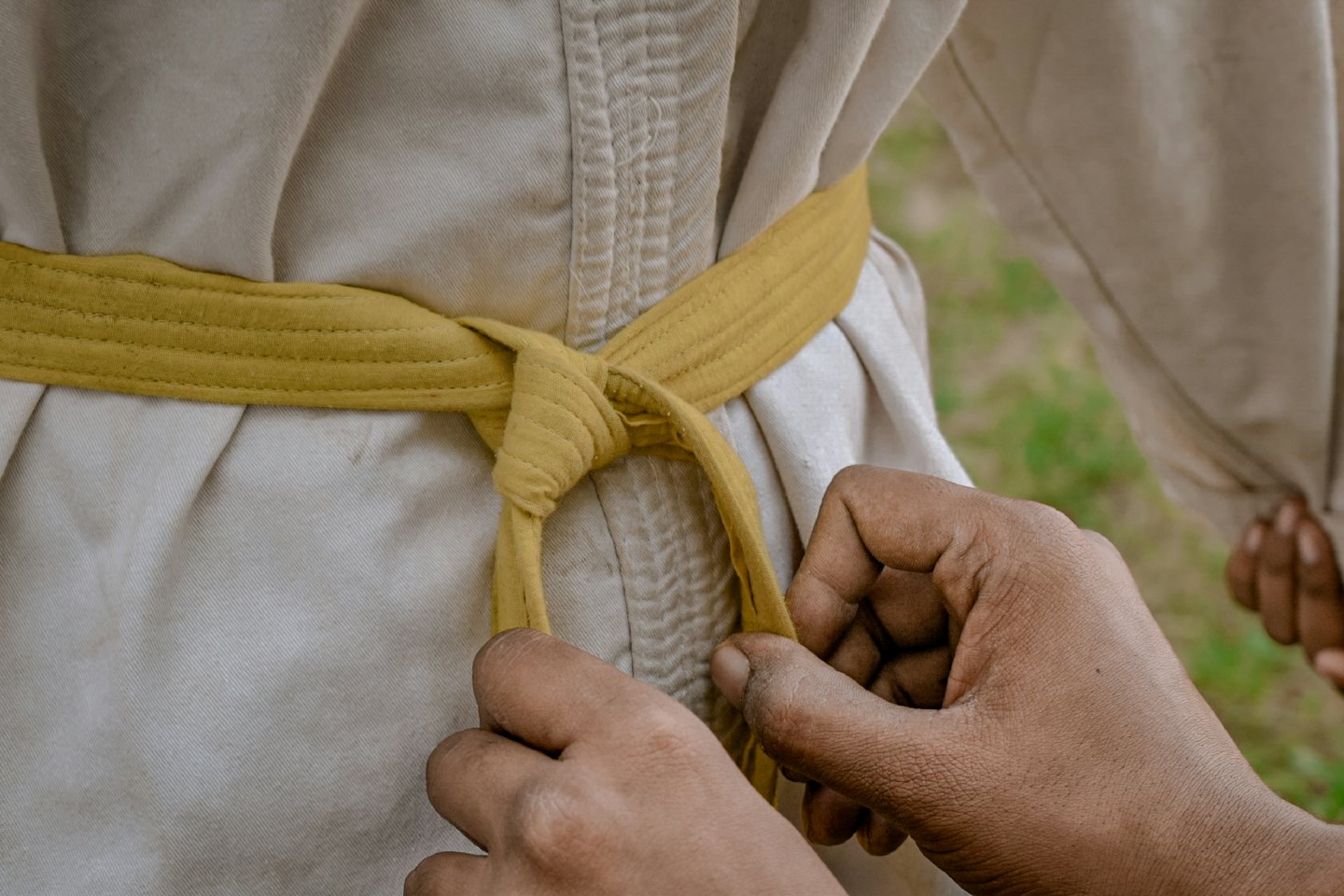 Mani che legano una cintura gialla di arti marziali su un judogi.